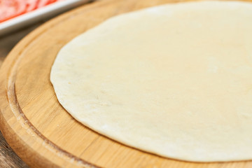 Unbaked piza dough sheet on wooden board, close up. Round pizza sheet on board.