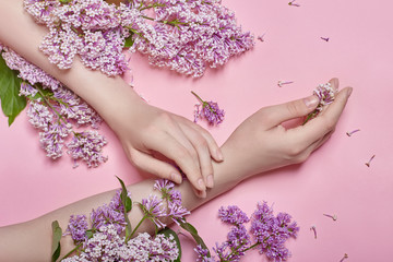 Obraz na płótnie Canvas Hands and spring flowers are on a pink table skincare. Nature Cosmetics for hand skin care, a means to reduce wrinkles on hands, moisturizing. Natural cosmetics from flower extract, beauty and fashion