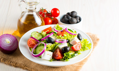 Fresh Greek salad made of cherry tomato, ruccola, arugula, feta, olives, cucumbers, onion and spices. Caesar salad in a white bowl on wooden background. Healthy organic diet food concept.