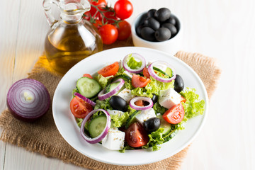 Fresh Greek salad made of cherry tomato, ruccola, arugula, feta, olives, cucumbers, onion and spices. Caesar salad in a white bowl on wooden background. Healthy organic diet food concept.