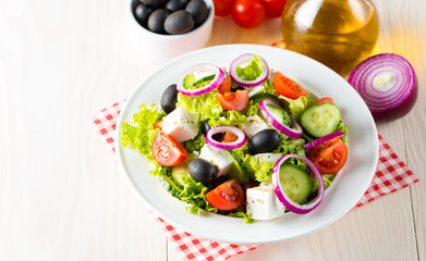 Fresh Greek salad made of cherry tomato, ruccola, arugula, feta, olives, cucumbers, onion and spices. Caesar salad in a white bowl on wooden background. Healthy organic diet food concept.