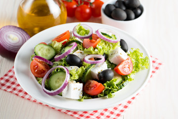 Fresh Greek salad made of cherry tomato, ruccola, arugula, feta, olives, cucumbers, onion and spices. Caesar salad in a white bowl on wooden background. Healthy organic diet food concept.