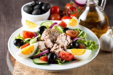 Fresh fish tuna salad made of tomato, ruccola, tuna, eggs, arugula, crackers and spices. Caesar salad in a white bowl on wooden background