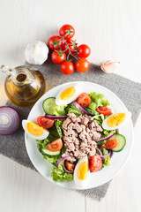 Fresh fish tuna salad made of tomato, ruccola, tuna, eggs, arugula, crackers and spices. Caesar salad in a white bowl on wooden background