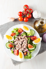 Fresh fish tuna salad made of tomato, ruccola, tuna, eggs, arugula, crackers and spices. Caesar salad in a white bowl on wooden background
