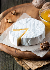 Brie type of cheese. Camembert cheese. Fresh Brie cheese and a slice on a wooden board with nuts, honey and leaves. Italian, French cheese.