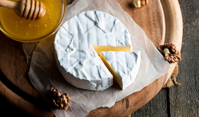 Brie type of cheese. Camembert cheese. Fresh Brie cheese and a slice on a wooden board with nuts, honey and leaves. Italian, French cheese.