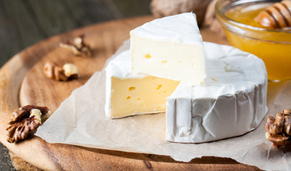Brie type of cheese. Camembert cheese. Fresh Brie cheese and a slice on a wooden board with nuts, honey and leaves. Italian, French cheese.
