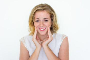 Fototapeta premium Emotional young pretty woman touching cheeks. Smiling lady. Sensitive woman concept. Isolated front view on grey background.