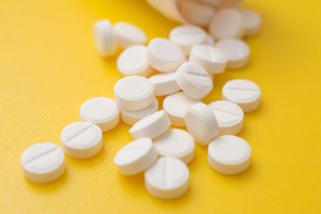 Fototapeta na wymiar White pills aspirin on yellow background, painkiller concept