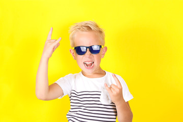 Cute blond boy wearing sunglasses showing Horns gesture