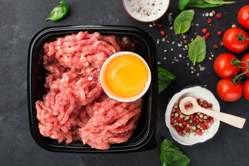 Raw minced meat with salt, pepper, egg, herbs, spices for a burger. On a dark background. Top view.