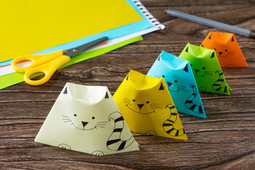 Origami toy made from paper puppets cat. Glue, scissors and paper on a wooden table. Children's art...