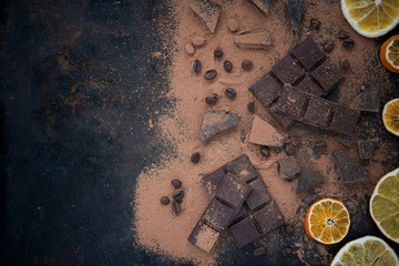 Chocolate bar with coffee beans,orange chips and cocoa powder on dark vintage background.Eye bird view.