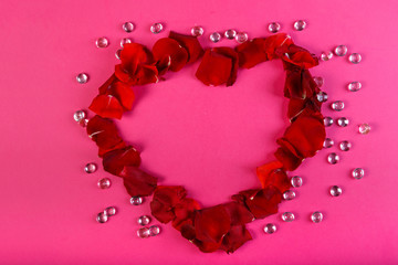 Heart of rose petals on a pink background decorated with white beads.