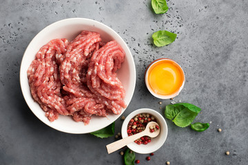 Fresh minced pork with egg, salt, pink pepper, cherry tomatoes on a light background with basil leaves. Top view.