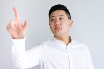 Serious Asian guy touching invisible wall. Handsome business man standing and advertising something. Promotion concept. Isolated front view on white background.