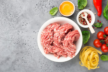 Fresh minced pork with egg, salt, pink pepper, cherry tomatoes on a light background with basil leaves. Top view.