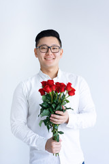 Smiling Asian man holding bunch of roses. Young man looking at camera. Flowers and gift concept. Isolated front view on white background.
