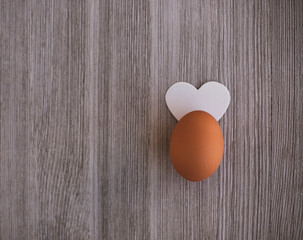 One Organic Brown Chicken egg  Decorated  White Heart like Ears on a Wooden Table. Copy Space. Easter Concept.