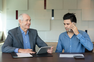 Glad senior businessman with junior officer. Smiling boss looking at young employee talking on phone. Business discussion concept
