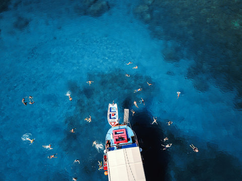 Aerial shot of beautiful blue lagoon at hot summer day with sailing boat. Top view of people swimming around the boat.