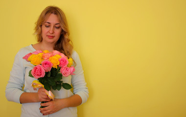 Beautiful blond girl in the blue dress holding bouquet of yellow and pink roses on a light-yellow background. Copyscape for your text.