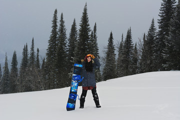 Young stilysh snowboarder girl stand on top of a mountain and holding her snowboard. Prepearing to...