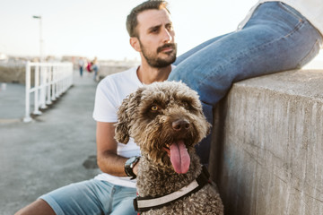 .Young and beautiful couple in love enjoying an afternoon outdoors near the port of Gijón, in Asturias (Spain). A fun and playful couple with their sweet Spanish Water Dog. Lifestyle. Love.