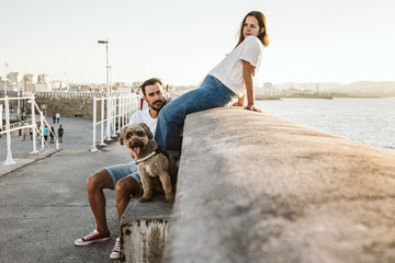 .Young and beautiful couple in love enjoying an afternoon outdoors near the port of Gijón, in Asturias (Spain). A fun and playful couple with their sweet Spanish Water Dog. Lifestyle. Love.