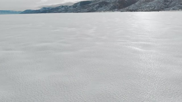 Aerial-Flying low and fast over pristine snow field reflecting low sunlight