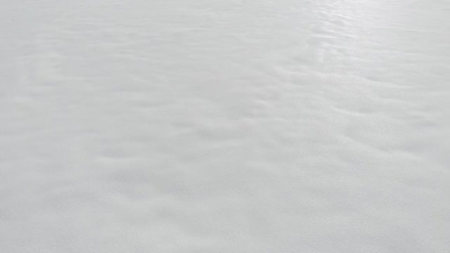 Aerial-Pull back low over textured snow field with no other elements in the frame