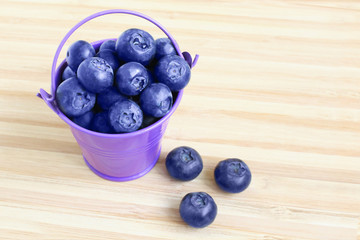 Fresh ripe blueberries in a small bucket on a wooden table with copy space for your text