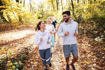 Small group of people running in woods in the autumn. In foreground couple smiling at each other.