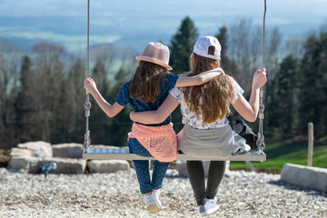 Two gorgeous blonde girls swinging on a swing on a sunny summer day
