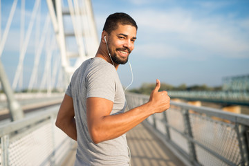 Smiling athlete with earphones holding thumbs up ready for training. Running and fitness lifestyle.