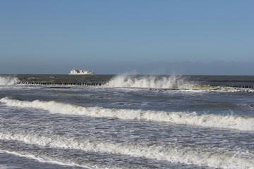 big splashing waves in the sea in winter with a ship in the background