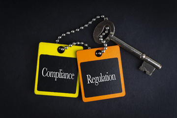COMPLIANCE REGULATION inscription written on wooden tag and key on black background with selective focus and crop fragment. Business and education concept