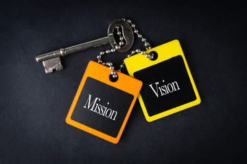 MISSION VISION inscription written on wooden tag and key on black background with selective focus and crop fragment. Business and education concept