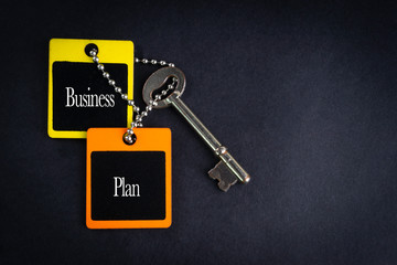 BUSINESS PLAN inscription written on wooden tag and key on black background with selective focus and crop fragment. Business and education concept