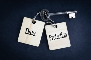 DATA PROTECTION inscription written on wooden tag and key on black background with selective focus...