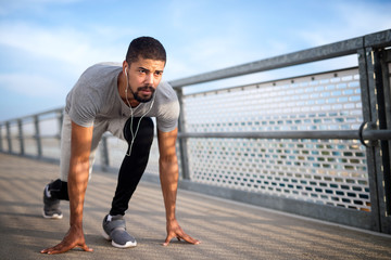 Young focused sporty person with earphones in low start position for sprint. 