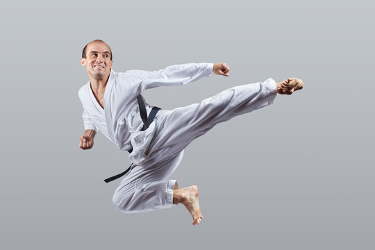 Adult man performs a kick to the side in a jump on a gray background