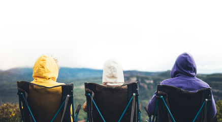 three friends sit in camping chairs on top of a mountain, travelers enjoy nature, tourists look...