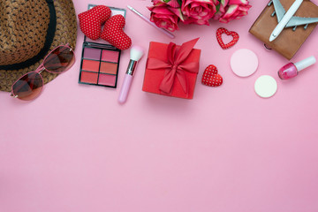 Table top view aerial image of decoration valentine's day background concept.Flat lay essential items red heart & gift box on modern rustic pink paper with clothing women & cosmetic for travel.