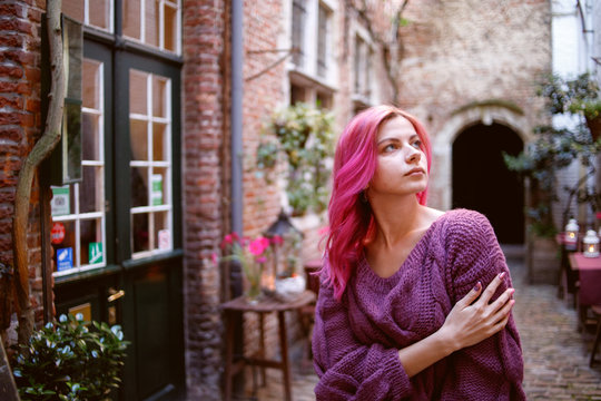 A young, beautiful girl with pink hair walks through the old stone yard.