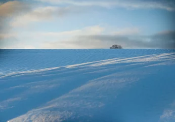 Fotobehang Field covered with snow waves. Winter hill at sunset. © ala