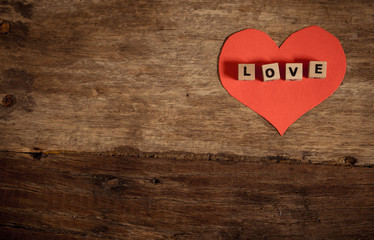 Love text written with wood blocks on red heart on rustic vintage background