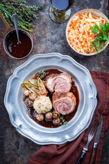Traditioneller Wildschwein Rollbraten mit Semmelknödel und gebratenen Chicoree Salat  als Draufsicht in Rotwein Sauce auf einem Zinnteller 