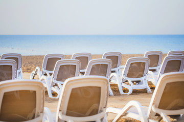 Summer morning empty sunny beach with white plastic chairs for sunbathing. Happy summer vacations concept. Horizontal color image.
